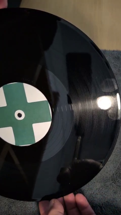 Fingerprint and light haze are visible on a vinyl record under angled light.
