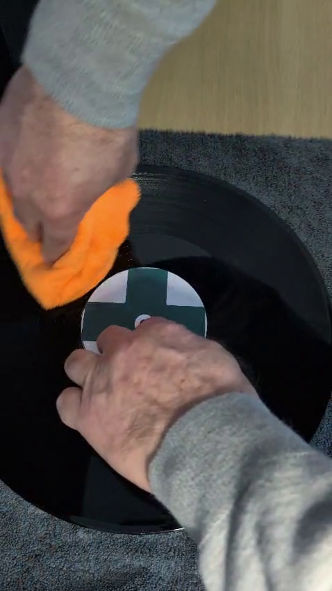 Wiping a vinyl record gently along the groove direction with a microfibre cloth.